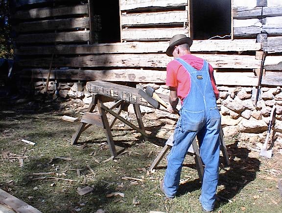 craftsman using a broad ax to hand hewn logs